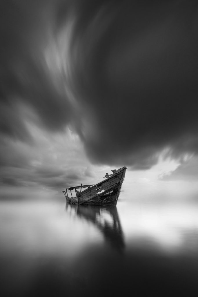 Abandoned shipwreck on a calm lake with a dramatic sky in Makassar, Indonesia.